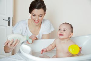 Mum pouring soap on hand, baby in bathtub