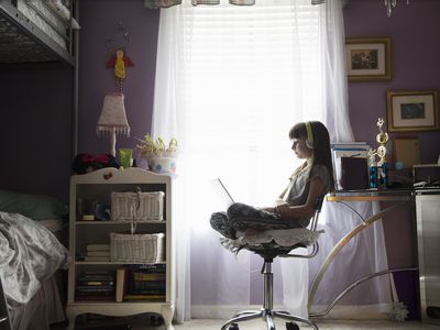 Young girl in bedroom using laptop with headphones