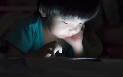 孩子晚上在黑暗的床上用平板电脑阅读。
