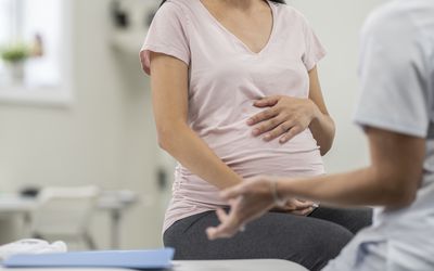 image of a pregnant person holding belly and sitting on a doctor's table