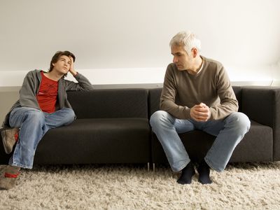 teenage boy rolling his eyes and sitting on couch with father