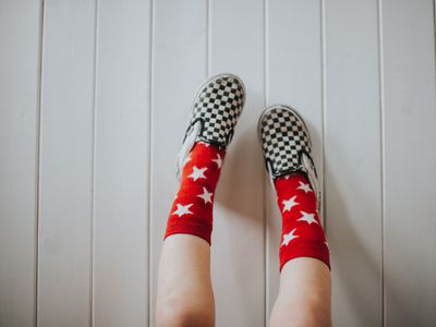 Feet clad in Vans Kids' Checkerboard Classic Slip-On set against a white wooden surface