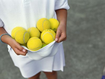 kid holding a bunch of tennis balls