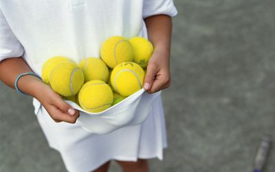 kid holding a bunch of tennis balls