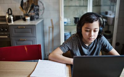 男孩在家里写作业时戴着耳机使用笔记本电脑
