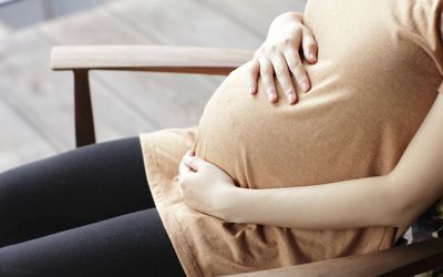 孕妇怀孕后坐在椅子上，手放在肚子上