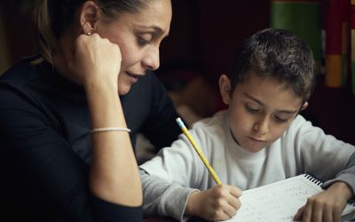 一位母亲坐在她的孩子旁边，帮助他做家庭作业。