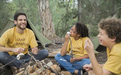 A camp counselor and two kids eating fried marshmallows