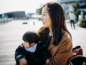 年轻的亚洲单身母亲抱着可爱的小女儿，坐在户外码头边沉思