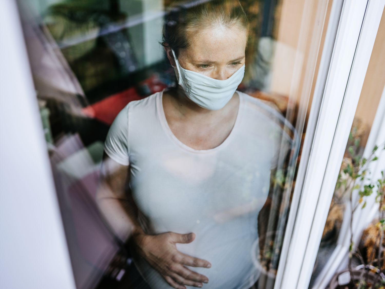 Pregnant woman with mask looking out window