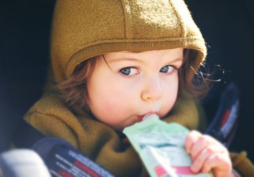 近距离的肖像甜美的蹒跚学步的孩子吃水果泥从塑料doy包，坐在婴儿车，户外零食时间