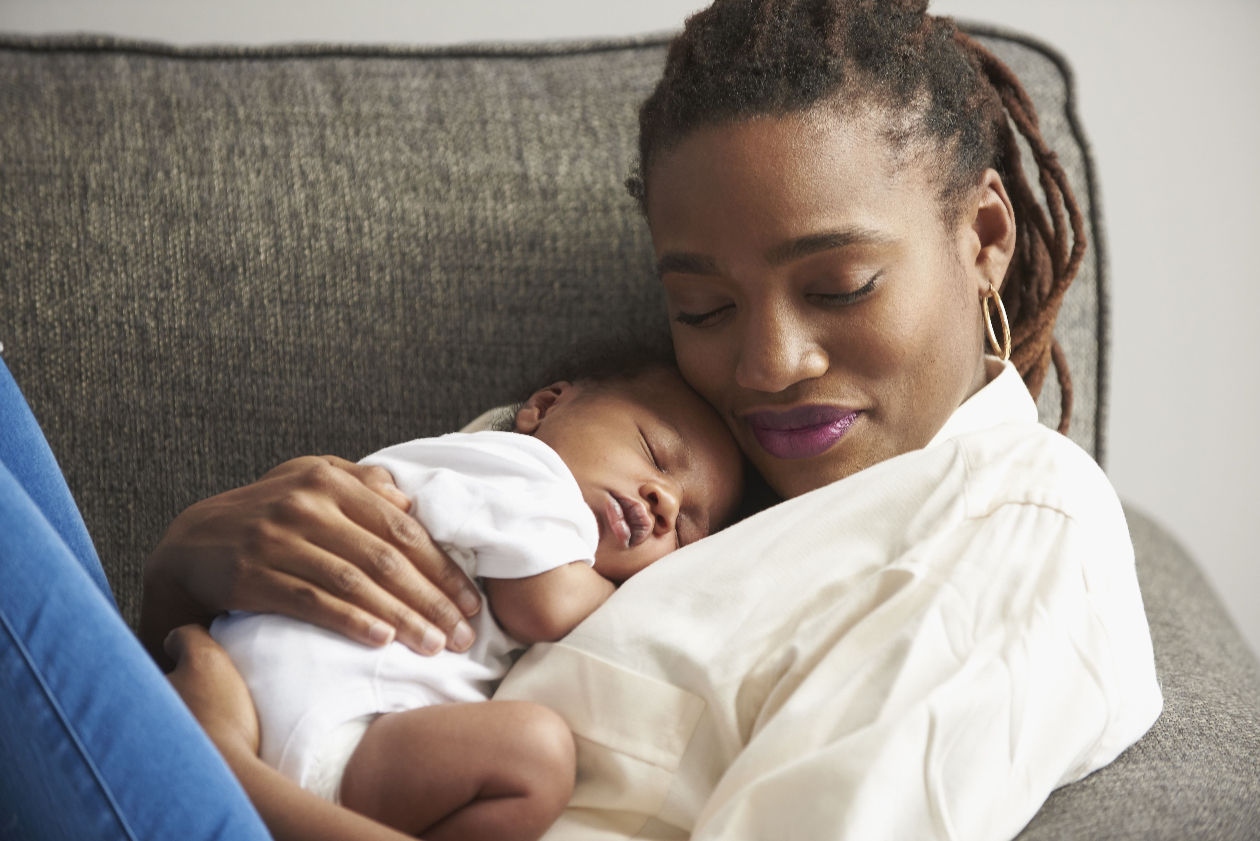 黑人母亲抱着睡在沙发上的婴儿儿子