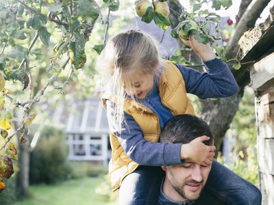 Daughter on fathers shoulders, picking apple from tree