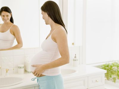 Pregnant woman with hands on stomach looking in mirror.