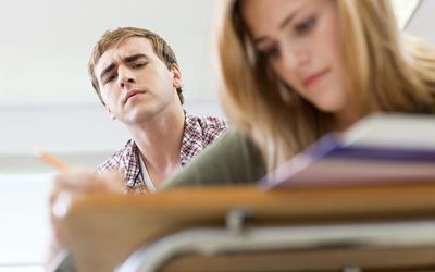 Teen looking cover classmate's shoulder at paper