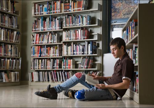 一个十几岁的男孩在图书馆的地板上看书