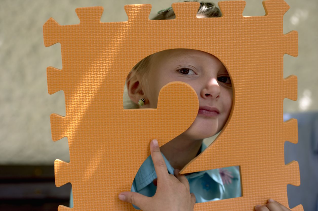 Little girl holding the foamed plastic frame of a number in front of her face