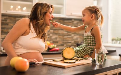 Little girl feeding pineapple to pregnant mom