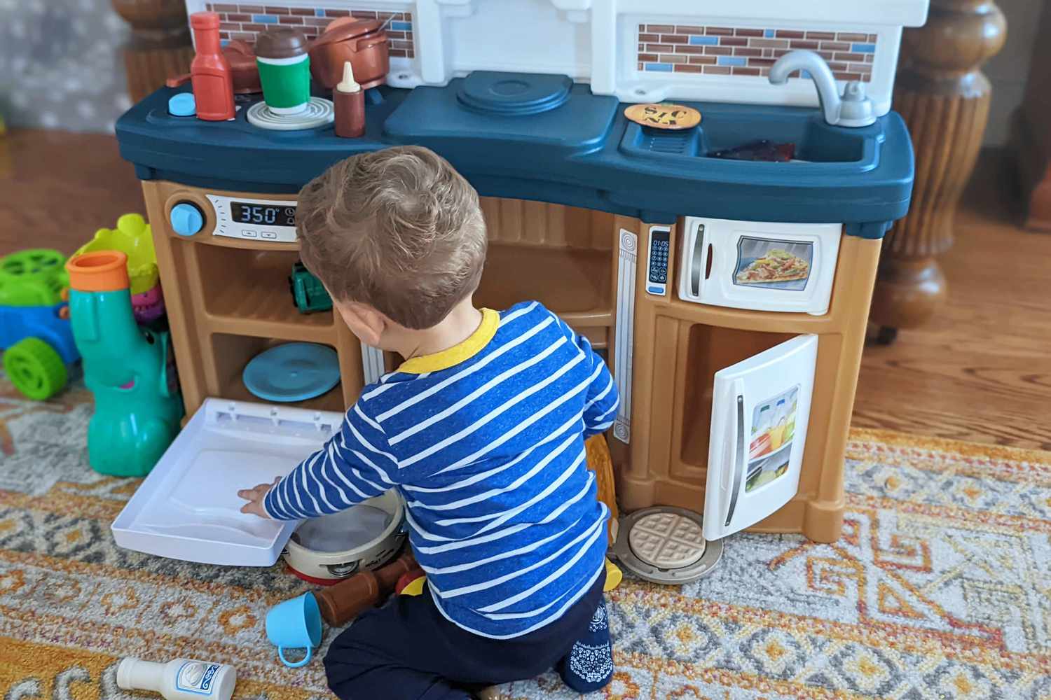 Toddler playing with Step2 Fun with Friends Kitchen displayed on carpet