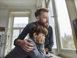 father with arm around son looking out window