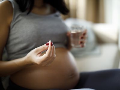 Pregnant woman holding a white pill and a glass of water