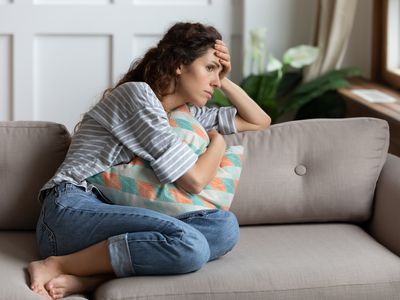 Sad woman sitting on the couch holding a pillow.