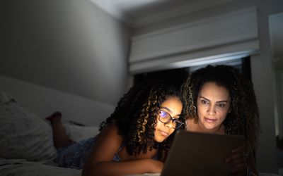 母亲和女儿在床上使用平板电脑