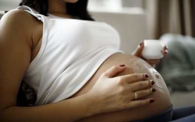 孕妇在腹部涂抹局部药膏的图像。