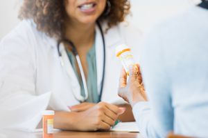 Close up of a patient holding pill bottle talking to a doctor