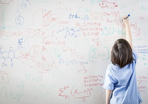 Schoolgirl writing on a dry erase board full of math equations