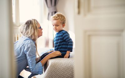 A mother talking to her toddler son inside in a bedroom