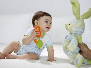 女婴(15-18个月)坐在床上，男人的手拿着玩具兔子