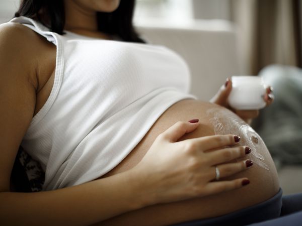 Image of a pregnant person applying a topical cream to belly.