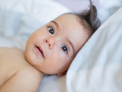 Baby boy laying on white bed looking at camera