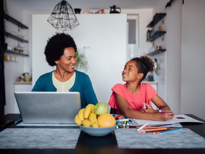 A happy African American family, mature mother working from home on her laptop, while her daughter is homeschooling and doing her homework