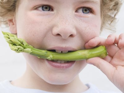 男孩biting a spear of asparagus