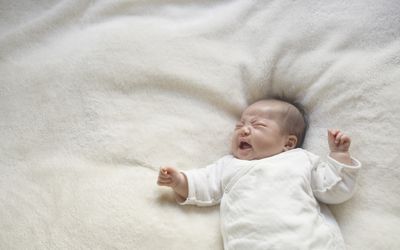 亚洲婴儿在白色毯子上哭泣。