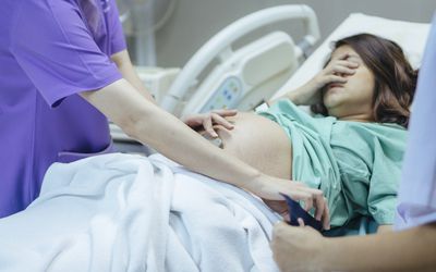 分娩妇女在医院病床上用手捂住她的脸，护士检查她。