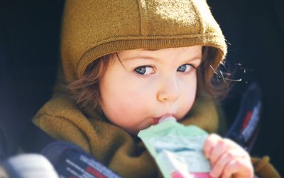近距离的肖像甜美的蹒跚学步的孩子吃水果泥从塑料doy包，坐在婴儿车，户外零食时间