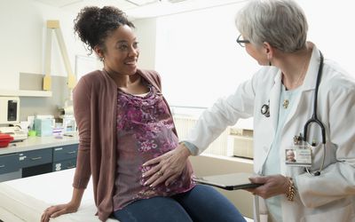 pregnant woman sitting on examining table while doctor touches her stomach