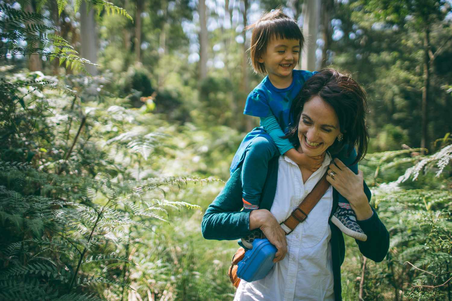 Child on mother's shoulders while walking through the forest