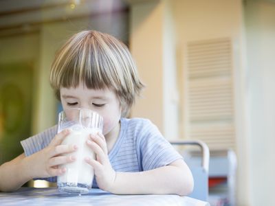 Young child drinking large glass of milk