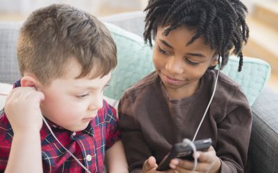 Boys sharing headphones and cell phone on sofa