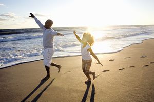 A father and daughter pretend to fly on the beach on a sunny day near the ocean.