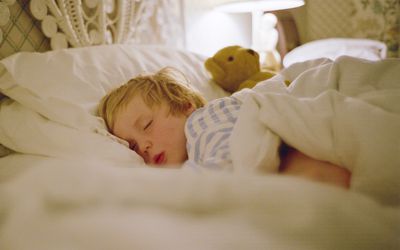 young boy asleep in a bed with a teddy bear