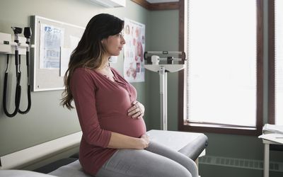 Pensive pregnant woman holding stomach in examination room