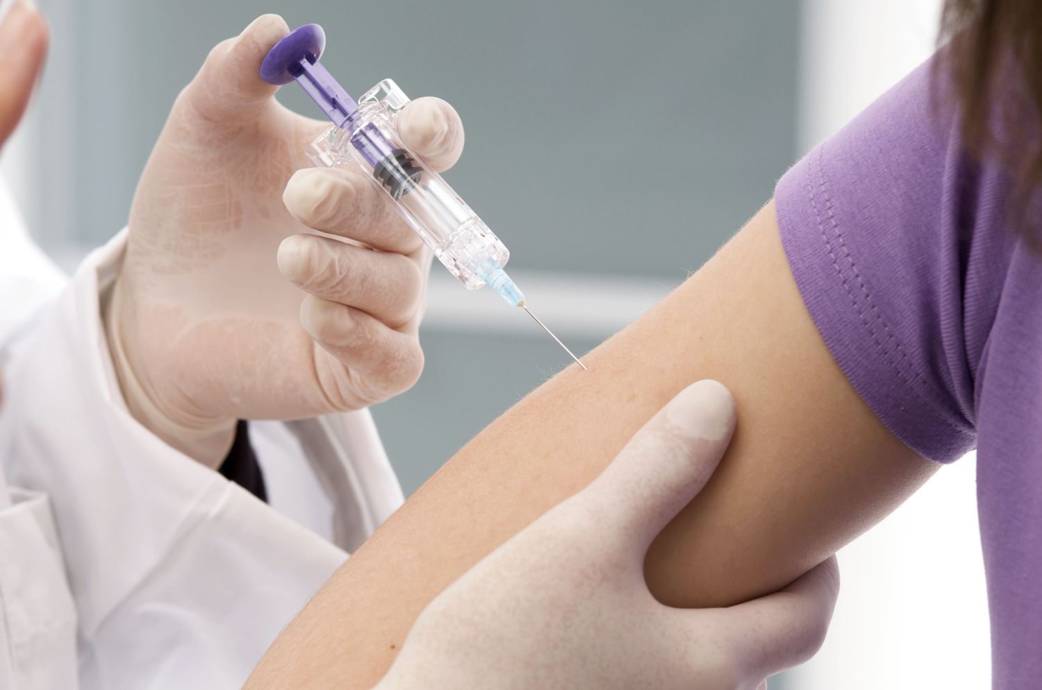 Woman receiving injection in her arm from gloved hands