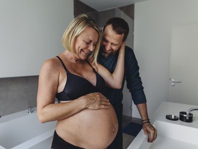 Happy mature pregnant couple watching expectant mother's belly in bathroom