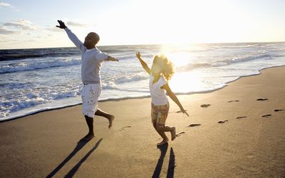 A father and daughter pretend to fly on the beach on a sunny day near the ocean.