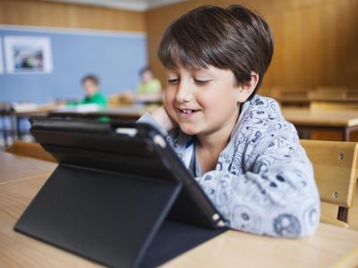 Happy schoolboy looking at digital tablet in classroom